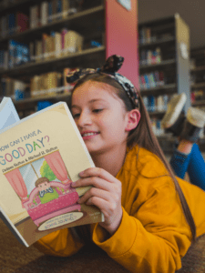 happy-girl-reading-a-book-mockup-lying-on-the-library-s-floor